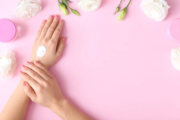 Young woman applying hand cream on color background