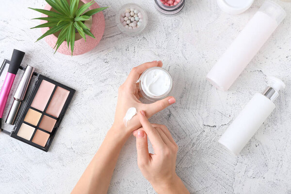 Young woman applying hand cream at table