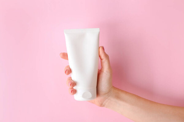 Female hand with tube of cream on color background