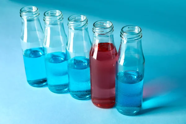 Jedna láhev s červenou tekutinou mezi lahvemi s modrými vzorky na barevném pozadí. Koncept jedinečnosti — Stock fotografie