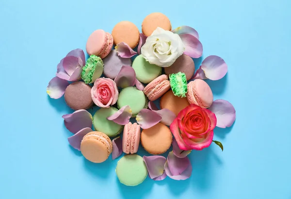 Tasty macarons with rose flowers on color background — Stock Photo, Image