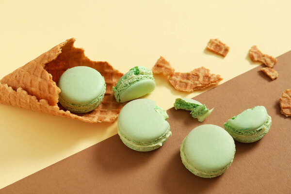 Wafer cone with tasty macarons on color background