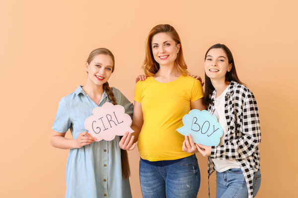 Лесбиянка пара и беременная женщина с написанными словами ДЕВУШКА и БОЙ на бумаге на цветном фоне. Концепция суррогатного материнства
