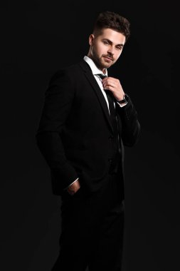 Siyah arka planda zarif takım elbiseli yakışıklı bir genç.