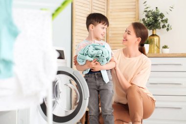 Küçük oğluyla birlikte evde çamaşır yıkayan genç bir kadın.