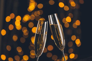 Bardakları şampanyayla tokuşturmak koyu arka planda bulanık ışıklarla