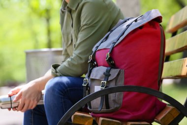 Sırt çantalı kadın gezgin parkta bankta oturuyor.