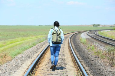 Sırt çantalı bir gezgin tren yolu boyunca yürüyor.