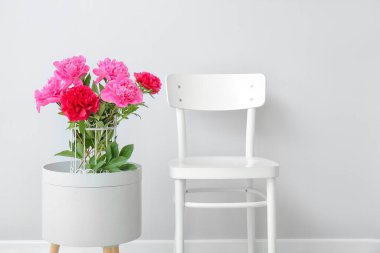 Masasında şakayık çiçekleri ve ışık duvarının yanında sandalyesi olan bir vazo.