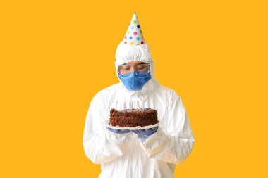 Asian man in biohazard suit and with Birthday cake on color background. Concept of epidemic clipart
