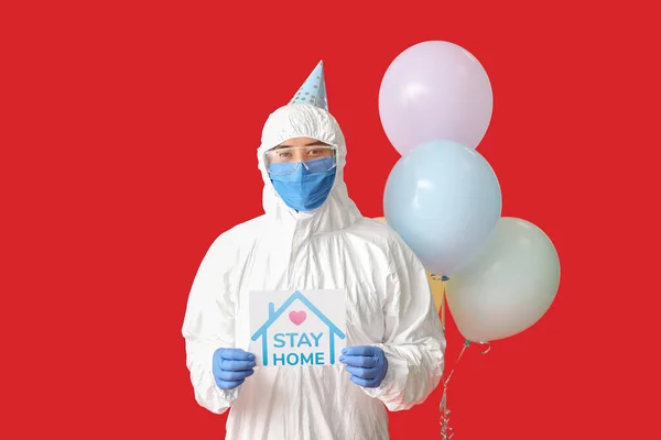 Asian man in biohazard suit and with Birthday balloons on color background. Concept of epidemic