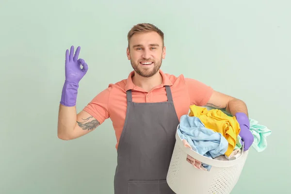 Young man with laundry showing OK gesture on grey background