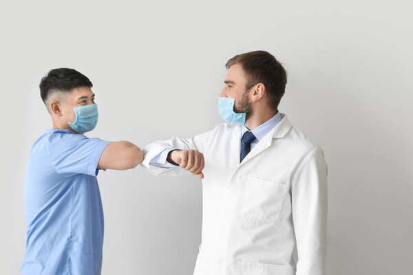 Young doctors greeting each other on light background. Concept of epidemic