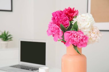 Masada güzel şakayık çiçekleri ve dizüstü bilgisayarı olan vazo.