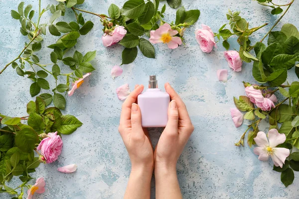 Female hands with perfume and flowers on color background