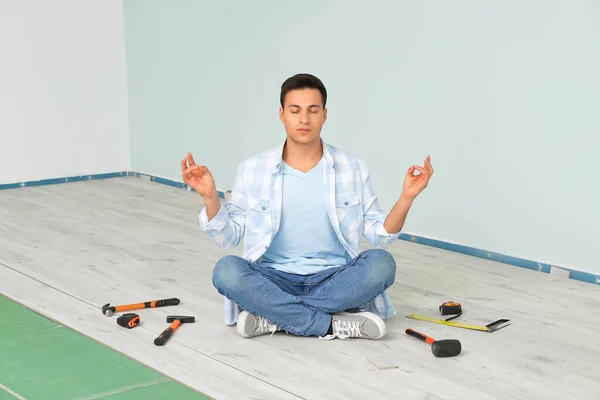 Meditating man during installing of laminate flooring in room