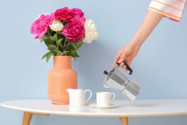 Bir kadın sıcak kahveyi fincandan fincana dolduruyor güzel şakayık çiçekleriyle.