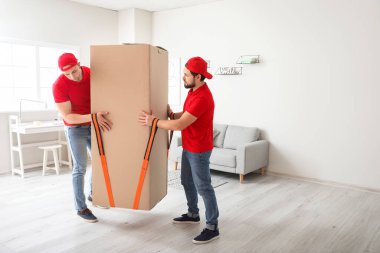 Yükleyiciler kargo kemeri kullanarak büyük bir kutu taşıyorlar.
