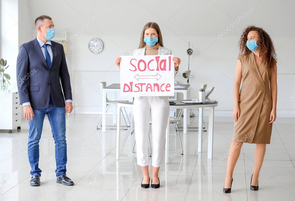 Colleagues with text SOCIAL DISTANCE on paper sheet in office. Concept of epidemic