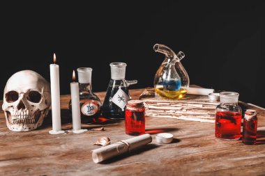 İksirler, insan kafatası, eski kitap ve mumlar simyacı masasında.