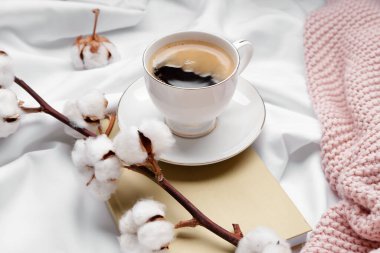 Bir fincan kahve, güzel bir pamuk dalı ve yatakta kitap.