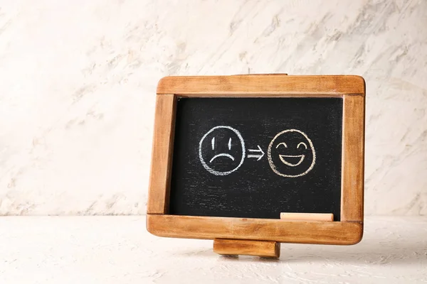 Chalkboard with drawn happy and sad faces on light background
