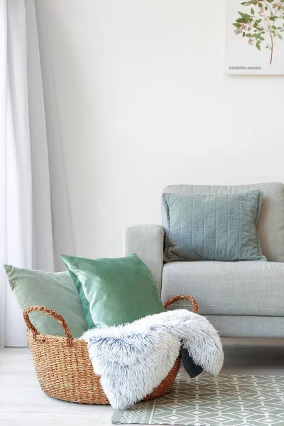 Wicker basket with pillows and plaid near sofa in room