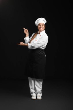 Genç bayan şef karanlık arka planda bir şeye işaret ediyor.