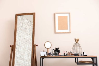 Odada dekoratif kozmetik seti ve ayna olan bir masa.