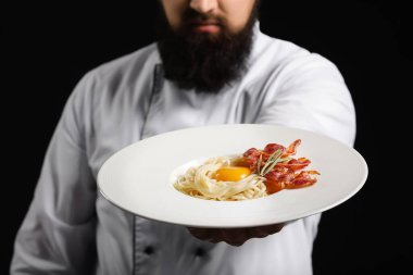 Siyah arka planda lezzetli makarna ile yakışıklı aşçı, yakın plan.