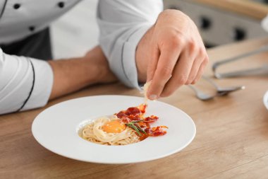 Erkek aşçı mutfakta lezzetli makarna pişiriyor, yakın plan.