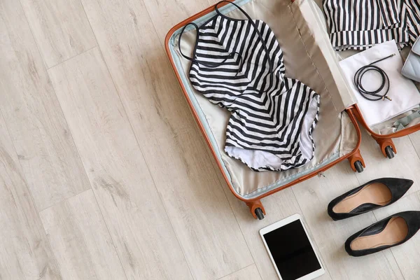 Open packed suitcase and accessories on wooden background