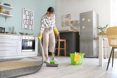 Mutfakta yerleri paspaslayan genç kadın.