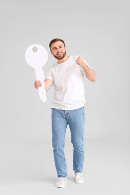 Gri arka planda büyük kağıt anahtarı olan mutlu genç adam.