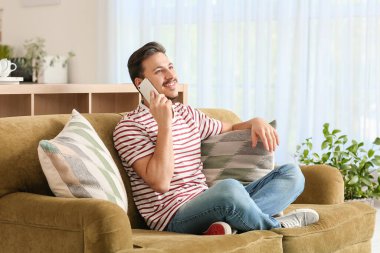 Yakışıklı genç adam evde telefonla konuşuyor.