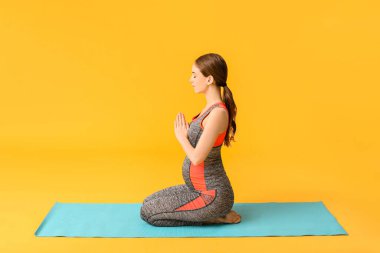 Genç hamile kadın arka planda yoga yapıyor.