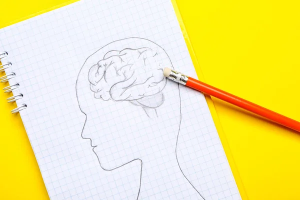 Notebook with drawing of human head and pencil with eraser on color background. Concept of dementia