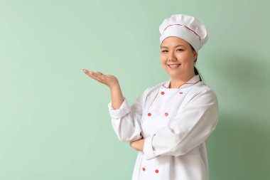 Güzel Asyalı şef renkli arka planda bir şeyler gösteriyor.