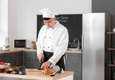 Yakışıklı Asyalı aşçı mutfakta yemek yapıyor.