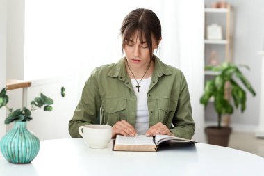 Evde İncil okuyan genç bir kadın.