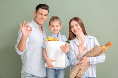 Çantasında yiyecek olan aile renk arkaplanında iyi bir jest gösteriyor