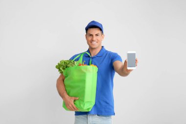 Paketinde yiyecek ve gri arka planda cep telefonu olan teslimatçı.