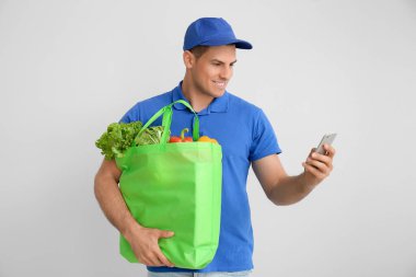 Paketinde yiyecek ve gri arka planda cep telefonu olan teslimatçı.