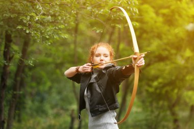 Sporty young woman practicing archery outdoors clipart