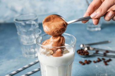 Bir bardak lezzetli dalgona kahveli ve arka planda kaşık renginde kadın eli.