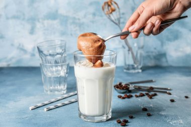 Bir bardak lezzetli dalgona kahveli ve arka planda kaşık renginde kadın eli.