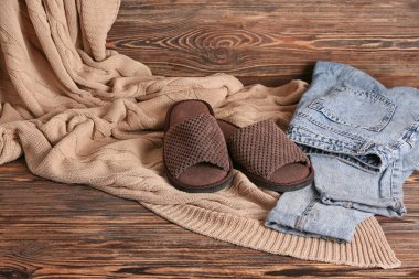 Bir çift yumuşak terlik ve ahşap arka planda giysiler.