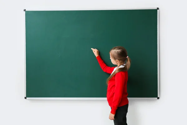 Cute little schoolgirl writing on blackboard in classroom