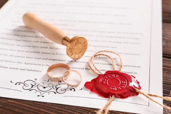 Marriage contract with wax seal stamp and wedding rings on table