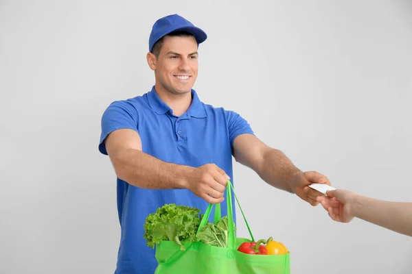 灰色の背景で顧客に注文する食品や名刺付きの袋を与える配達人 — ストック写真